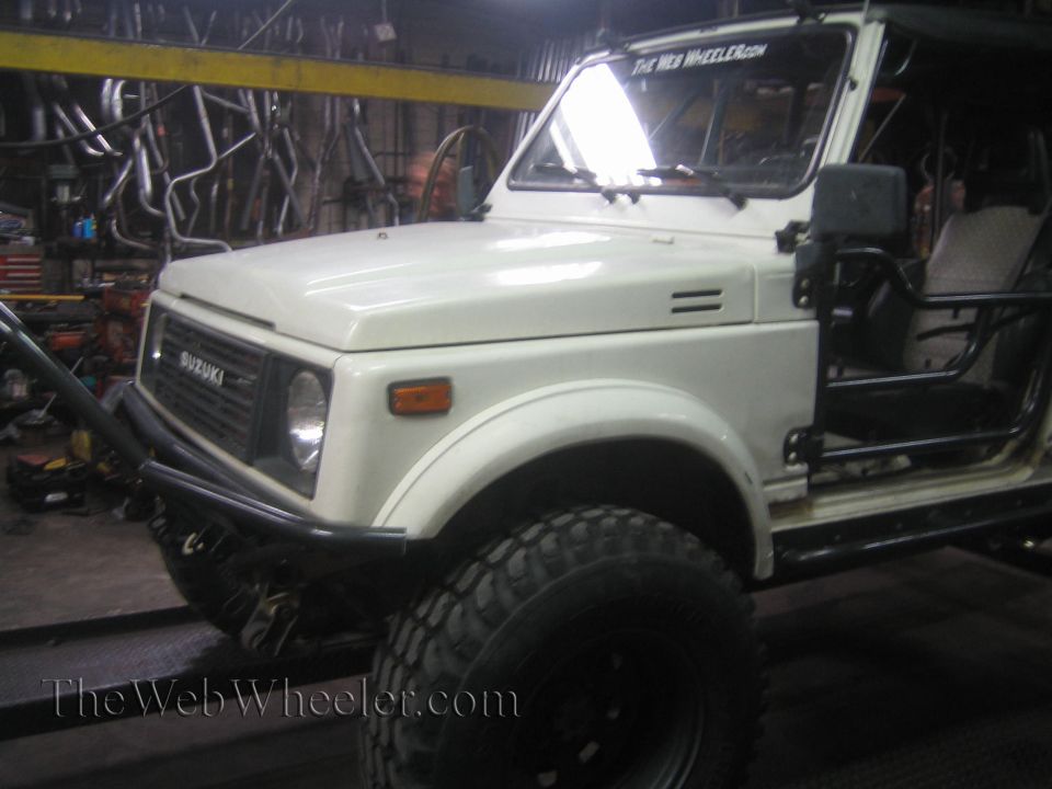 White 1987 Suzuki Samurai with aftermarket bumper and roll cage, parked indoors