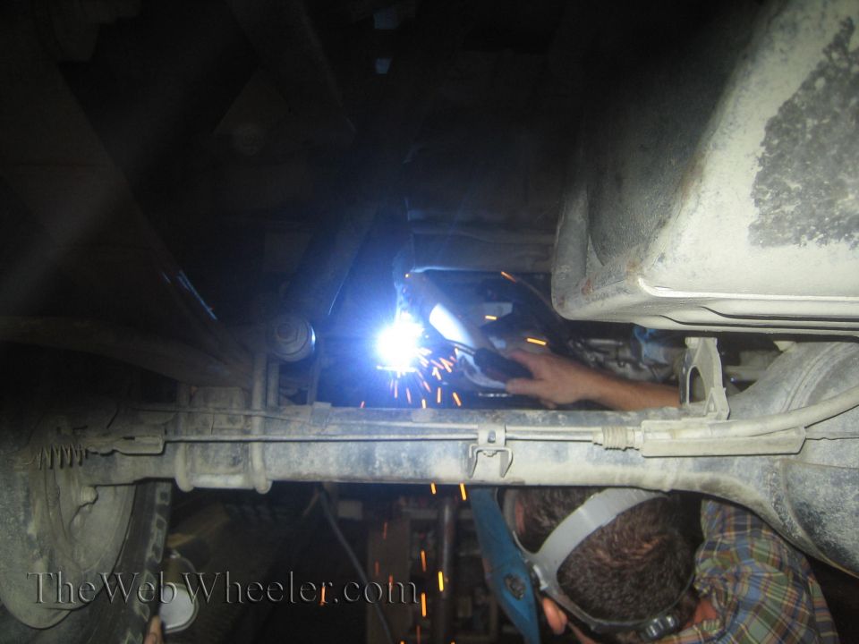 guy welding under car, sparks flying