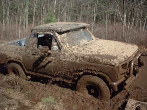 1978 Ford Bronco - This truck is deep in the mud, with trees in the background.