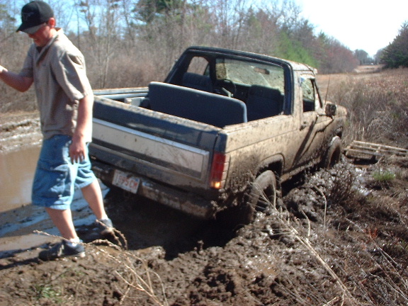 Mud-covered 1980s pickup truck stuck in mud, rear view