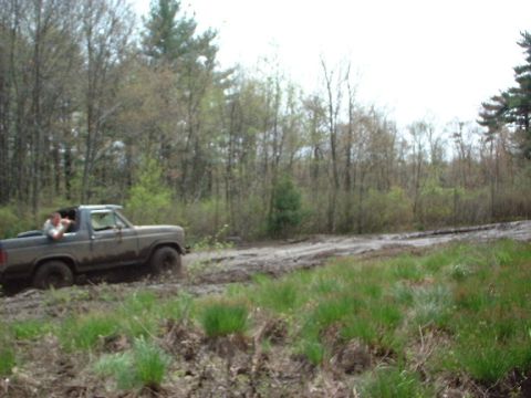 1978 Ford Bronco - A brown Ford Bronco navigates a muddy trail surrounded by trees.