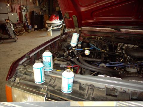 1988 Ford C-350 (Centurion Conversions) - Three cans of refrigerant and AC service equipment are placed on the fender of a maroon truck with its hood open.