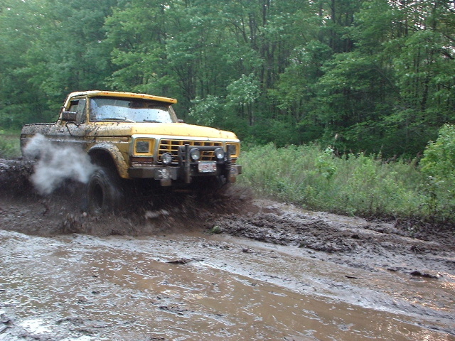 Yellow lifted Ford truck splashing through deep mud on a wooded trail