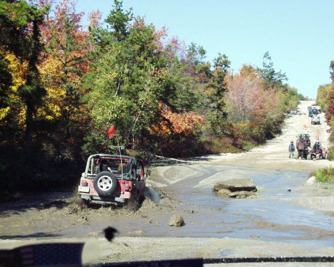 1989 Ford Bronco - Several off-road vehicles navigate a muddy trail during autumn.