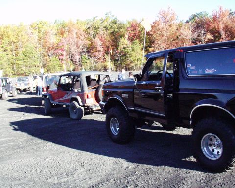 1989 Ford Bronco - A black Ford Bronco is parked next to other off-road vehicles on a sunny day.