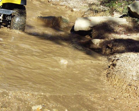 1989 Ford Bronco - Off-road vehicle navigates a muddy trail with rocks and water.