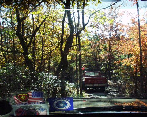 1989 Ford Bronco - A red Ford pickup truck navigates a rough, tree-lined path in the fall.