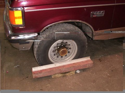 1988 Ford C-350 (Centurion Conversions) - Maroon Ford F-Series truck front fender and wheel. A metal alignment tool rests on blocks under the tire.
