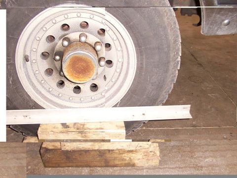 1988 Ford C-350 (Centurion Conversions) - A close-up view of a vehicle's wheel hub and tire, supported by wooden blocks, with visible rust on the hub.