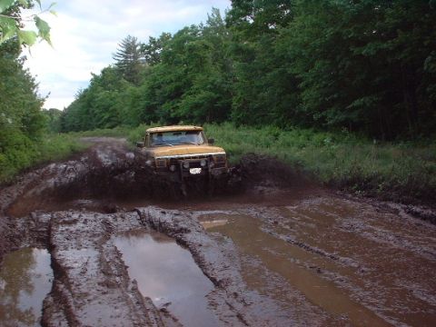 1978 Ford Bronco - A yellow 1978 Ford Bronco navigates a muddy trail, kicking up a large spray.