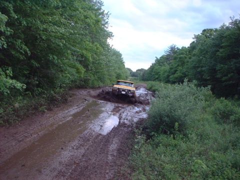 1978 Ford Bronco - A yellow SUV navigates a challenging muddy path, kicking up water and dirt.