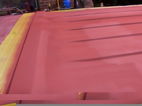 1988 Ford C-350 (Centurion Conversions) - A close-up view of a red painted surface, possibly a vehicle panel, with yellow masking tape along the edge.