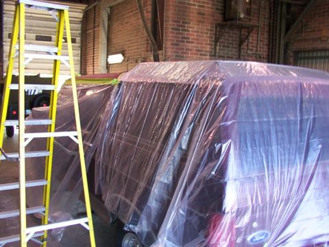 1988 Ford C-350 (Centurion Conversions) - A red vehicle, possibly a Ford, is covered in plastic sheeting, suggesting it is undergoing preparation for painting or repair.