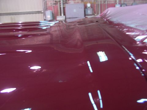 1988 Ford C-350 (Centurion Conversions) - Close-up of a shiny maroon vehicle hood, showing reflections of the surrounding environment.