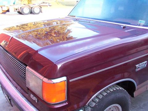 1988 Ford C-350 (Centurion Conversions) - Close-up of a maroon 1988 Ford C-350 (Centurion Conversions) truck, showing the hood, fender, and grille. A semi-truck is visible in the ba…