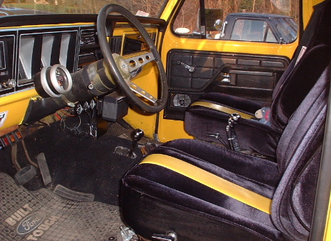 1978 Ford Bronco - The interior of a yellow Ford Bronco, black seats with yellow stripes and a visible floor mat with Ford branding.