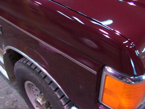 1988 Ford C-350 (Centurion Conversions) - A close-up view of the front corner of a maroon truck, highlighting the tire and headlight assembly.