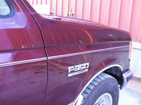 1988 Ford C-350 (Centurion Conversions) - The side view of a maroon Ford F-350 XLT Lariat truck shows its fender and part of the hood.