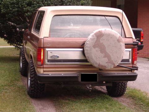 1985 Ford Bronco - The rear of a two-tone brown 1985 Ford Bronco is shown with a spare tire mounted on the back.