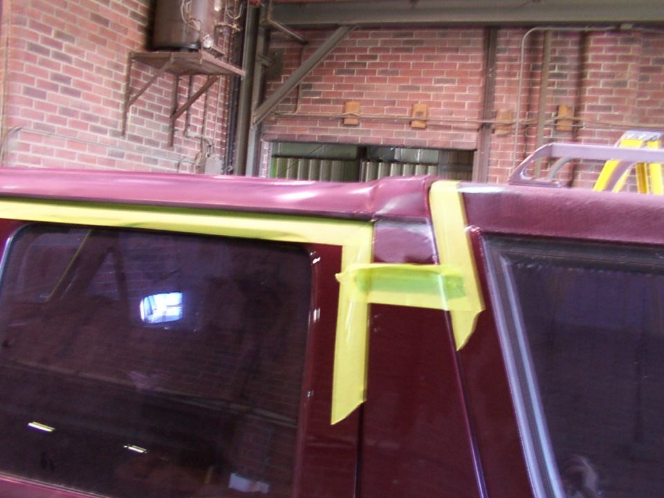 Maroon vehicle roofline with yellow masking tape on the B-pillar and window trim
