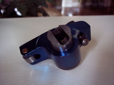 1963 Ford Galaxie - A close-up of a blue metal engine part, possibly a rocker arm, rests on a white surface.