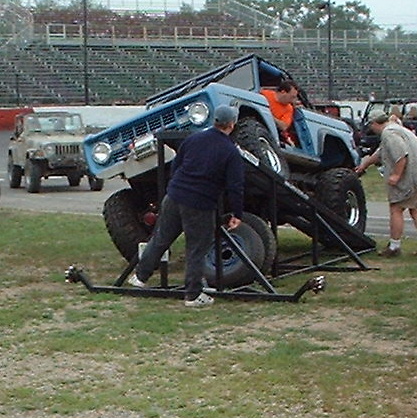 1978 Ford Bronco - A modified 1978 Ford Bronco is positioned on a ramp at an outdoor event, with spectators nearby and another vehicle in the background.