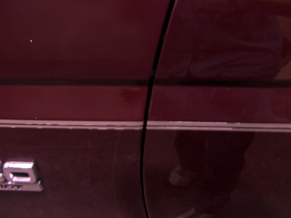Close-up of a dark red vehicle door with a chrome trim strip and a silver emblem that reads '5.0'