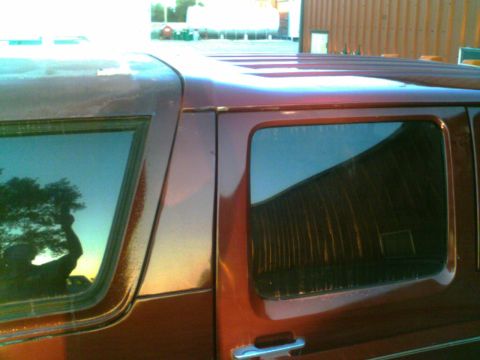 1988 Ford C-350 (Centurion Conversions) - Side view of a red van with peeling paint on the roof, reflecting a building in the window.