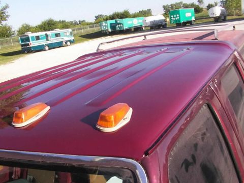 1988 Ford C-350 (Centurion Conversions) - The top of a red truck is visible, amber clearance lights and a roof rack. Other vehicles and trailers are in the background.