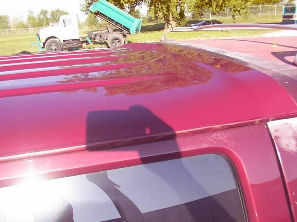 Red vehicle roof with a shadow of a person holding a phone. White dump truck in background