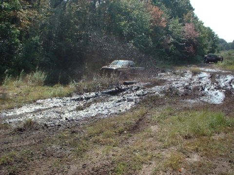 1978 Ford Bronco - A truck navigates a challenging muddy path, sending spray into the air.