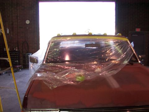1988 Ford C-350 (Centurion Conversions) - A vehicle is covered in plastic sheeting inside a garage, with a large open door in the background.
