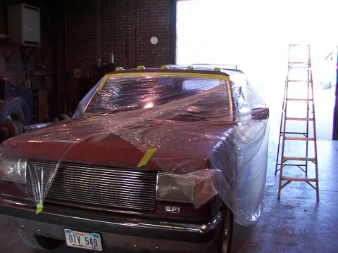 1988 Ford C-350 (Centurion Conversions) - A red pickup truck is covered in plastic wrap inside a garage, with a ladder nearby.