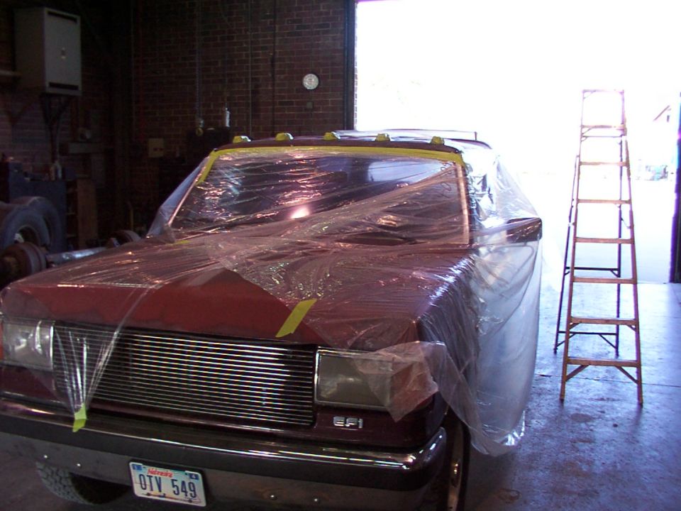 Red pickup truck covered in plastic wrap, front view, with chrome grille and headlights visible