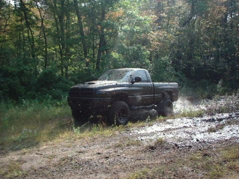 1978 Ford Bronco - A black pickup truck is stuck in the mud, kicking up spray as it attempts to move.