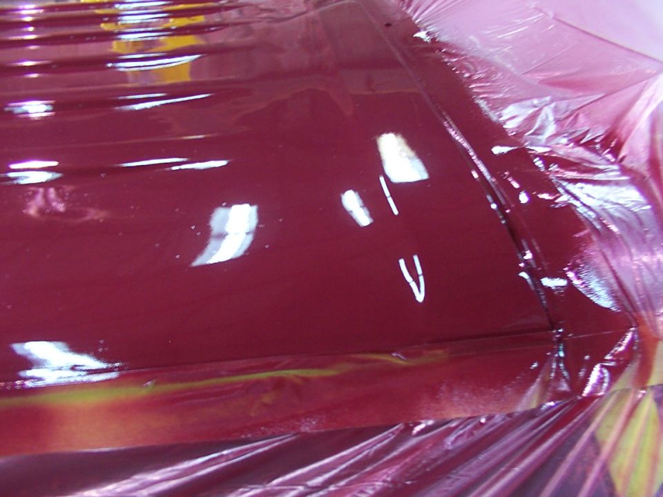 Close-up of a car roof with fresh red paint, covered in plastic sheeting