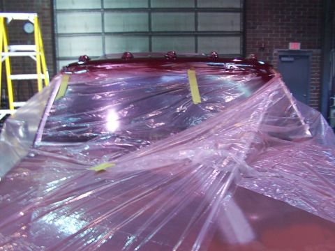 1988 Ford C-350 (Centurion Conversions) - The roof of a red truck is covered in plastic sheeting, likely for painting, with marker lights visible on top.