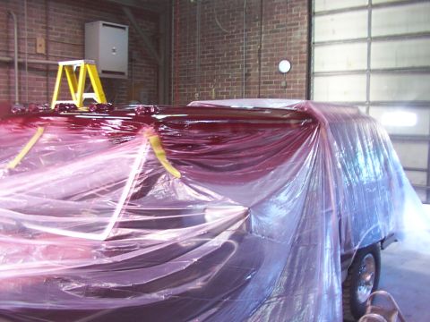 1988 Ford C-350 (Centurion Conversions) - Vehicle covered in plastic for painting inside a garage with a brick wall and large overhead door.