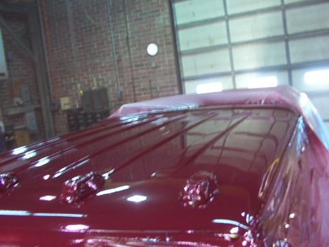 1988 Ford C-350 (Centurion Conversions) - The shiny red roof of a vehicle is covered in plastic wrap inside a garage.