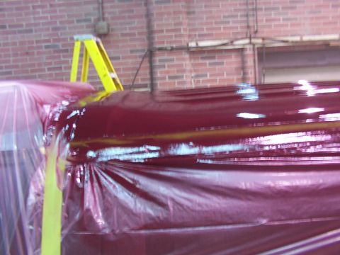 1988 Ford C-350 (Centurion Conversions) - A red vehicle's roof is covered in plastic sheeting, with a yellow ladder visible in the background.