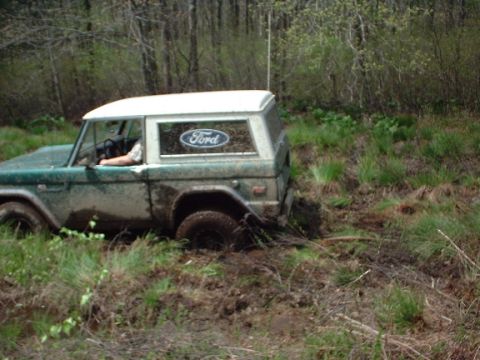 1978 Ford Bronco - A 1978 Ford Bronco is stuck in the mud off-road, with trees in the background.