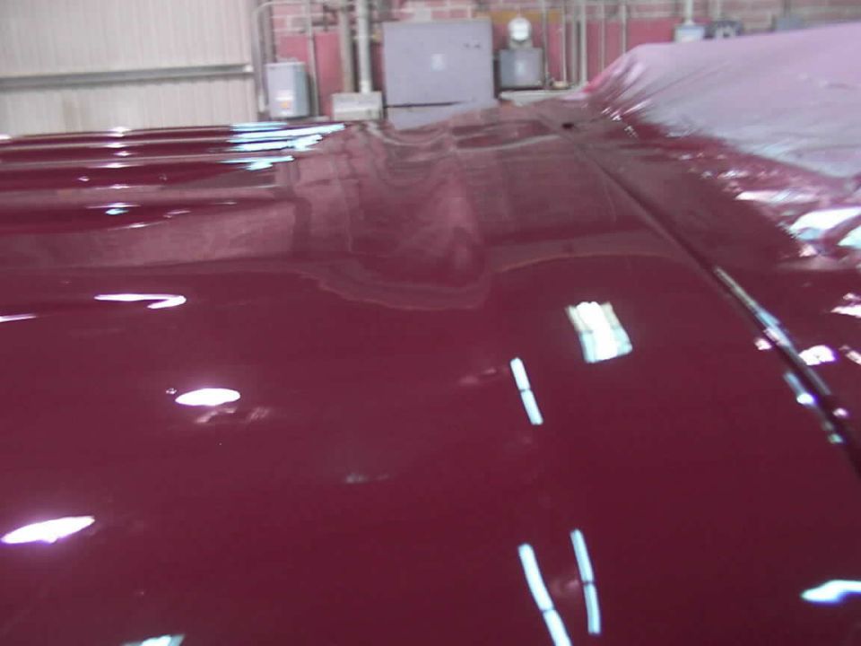 Maroon vehicle hood with reflections. Part of a vehicle is covered with a tarp