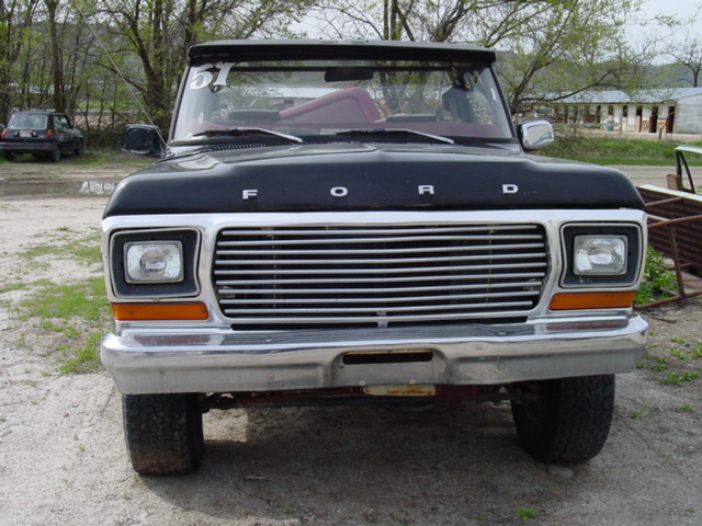 Front view of black Ford Bronco with chrome grille and bumper in gravel lot