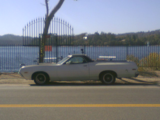 Silver Ford Ranchero car-pickup parked in side profile by a lake and iron fence