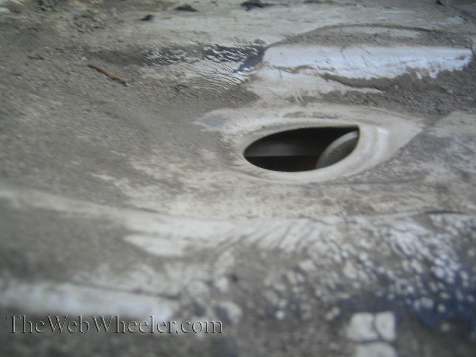 Underside of a vehicle showing a circular opening and some dirt