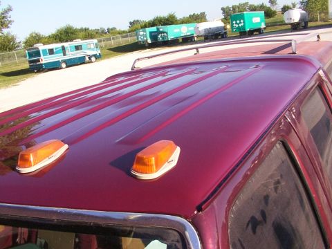 1988 Ford C-350 (Centurion Conversions) - The top of a maroon truck is visible, amber clearance lights and a roof rack. Several trailers and an RV are parked in the background.