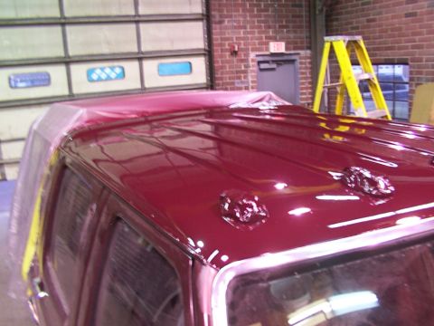 1988 Ford C-350 (Centurion Conversions) - The roof of a vehicle is being painted maroon, with plastic sheeting covering parts of it.