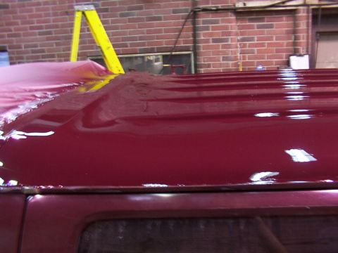 1988 Ford C-350 (Centurion Conversions) - The roof of a red van is visible, with a tarp partially covering it and a yellow ladder in the background.