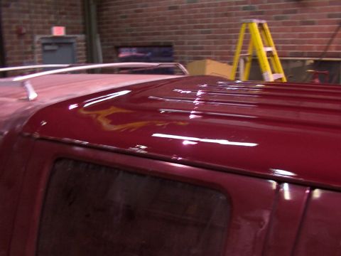 1988 Ford C-350 (Centurion Conversions) - The roof of a red van shows flame decals and a roof rack, with a ladder in the background.