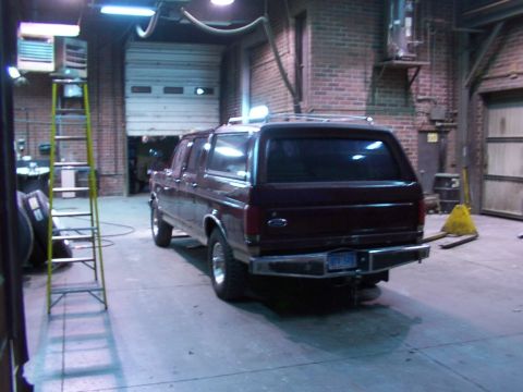 1988 Ford C-350 (Centurion Conversions) - A maroon extended cab pickup truck with a camper shell is parked inside a garage with the rear doors open.